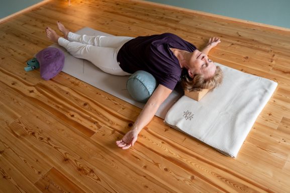 Eine Person liegt entspannt auf einer Yogamatte mit unterstützenden Kissen.